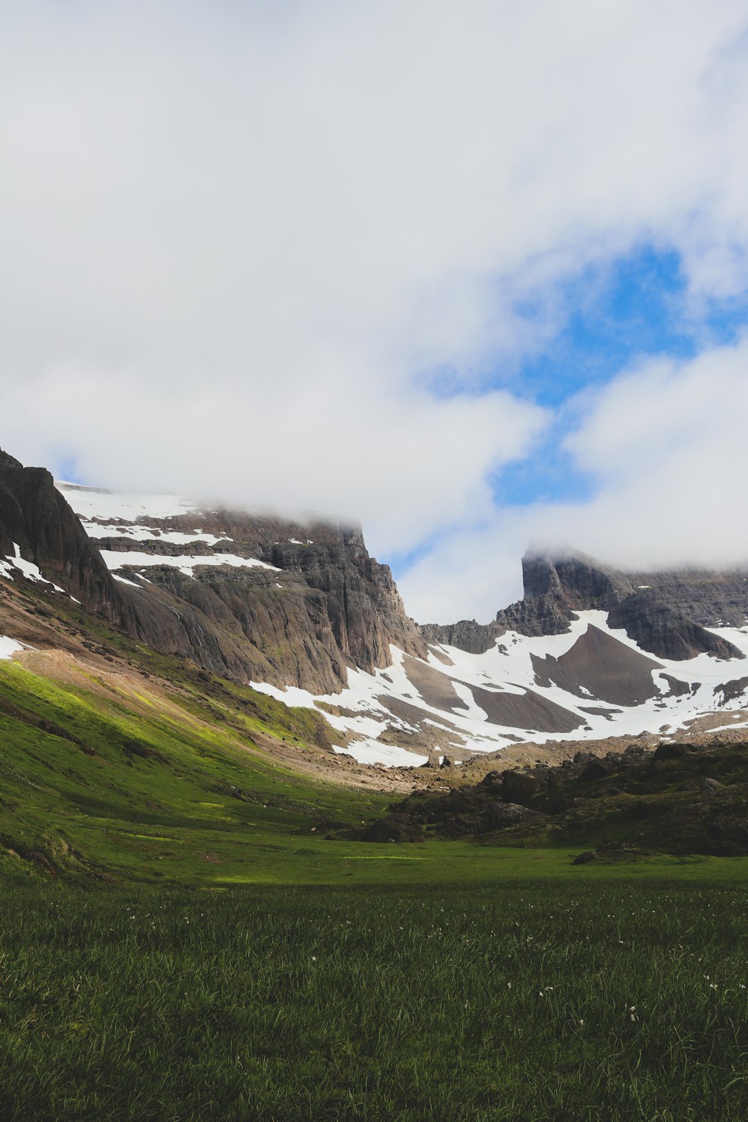 green grass field near snow covered mountain under cloudy sky during daytime