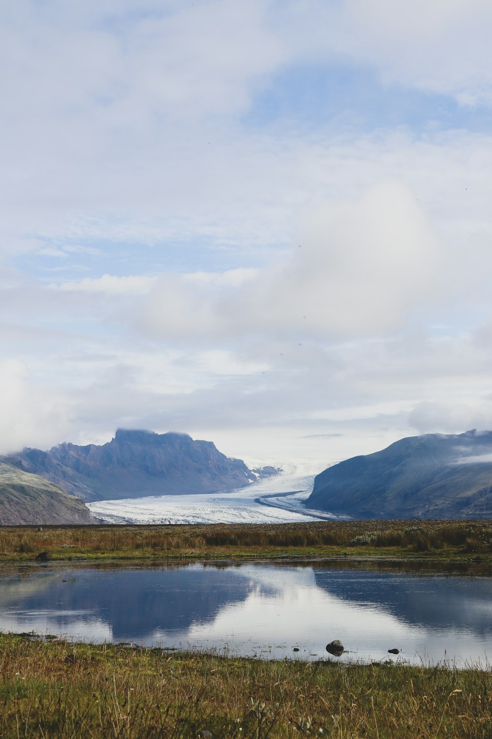 lake near mountain under white clouds during daytime