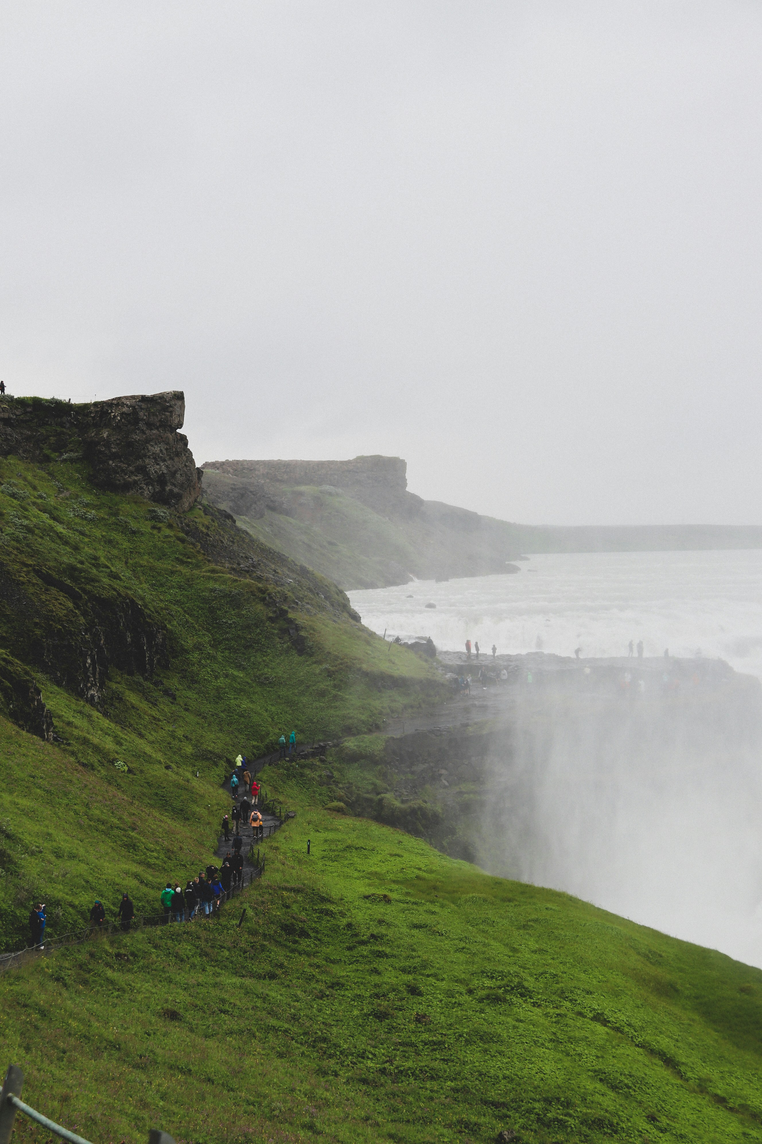 Persone che camminano sul campo di erba verde vicino allo specchio d'acqua durante il giorno