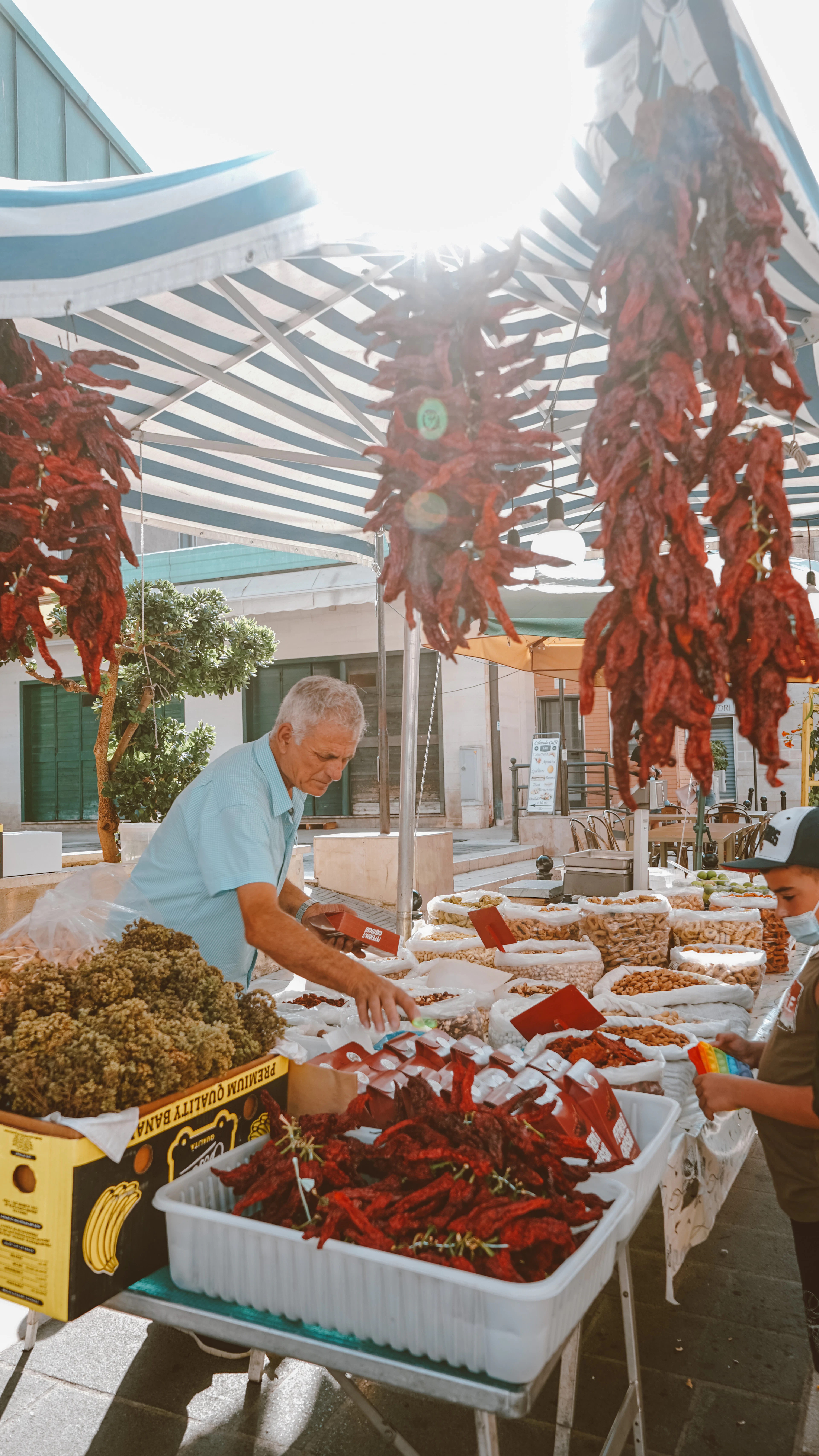 Strings of dried red peppers hanging over a food market stall in Matera, Italy, with crates of dried peppers, nuts and dried fruit spread out below