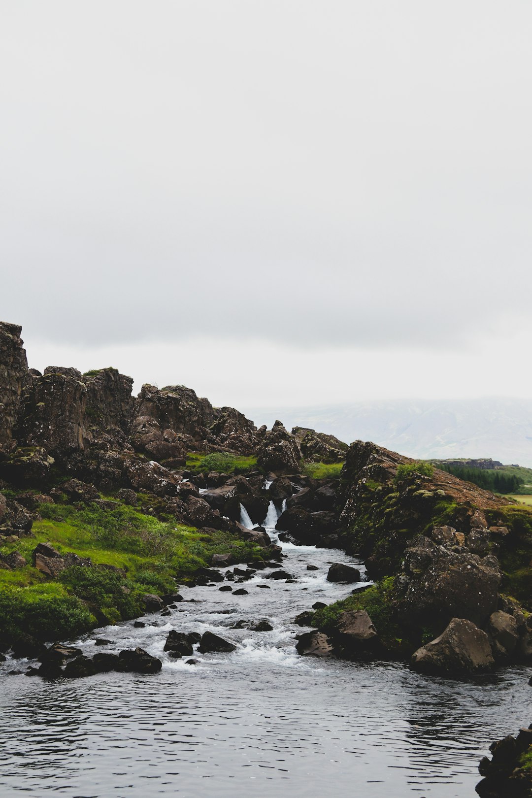 green and brown rocky mountain beside river under white sky during daytime