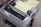 An Epson dot matrix printer with control buttons and a stack of continuous form paper loaded. The printer appears to be in an office or workspace setting.