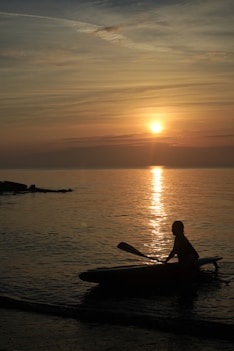 silhouette of man riding on boat during sunset