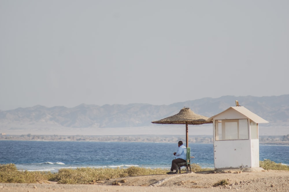 person in black shirt sitting on brown sand near body of water during daytime