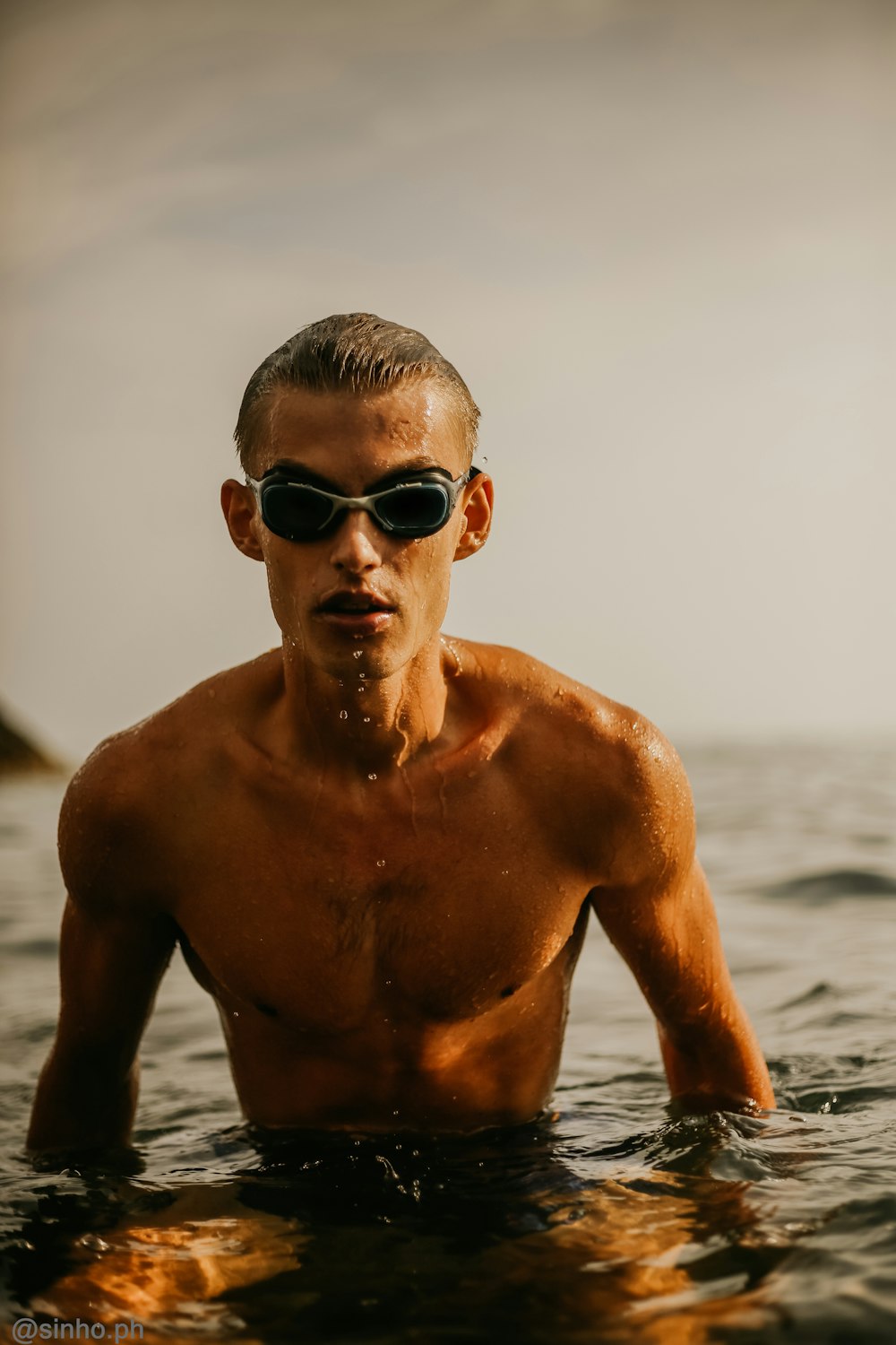 Hombre en topless con gafas de sol negras de pie en la orilla del mar durante el día