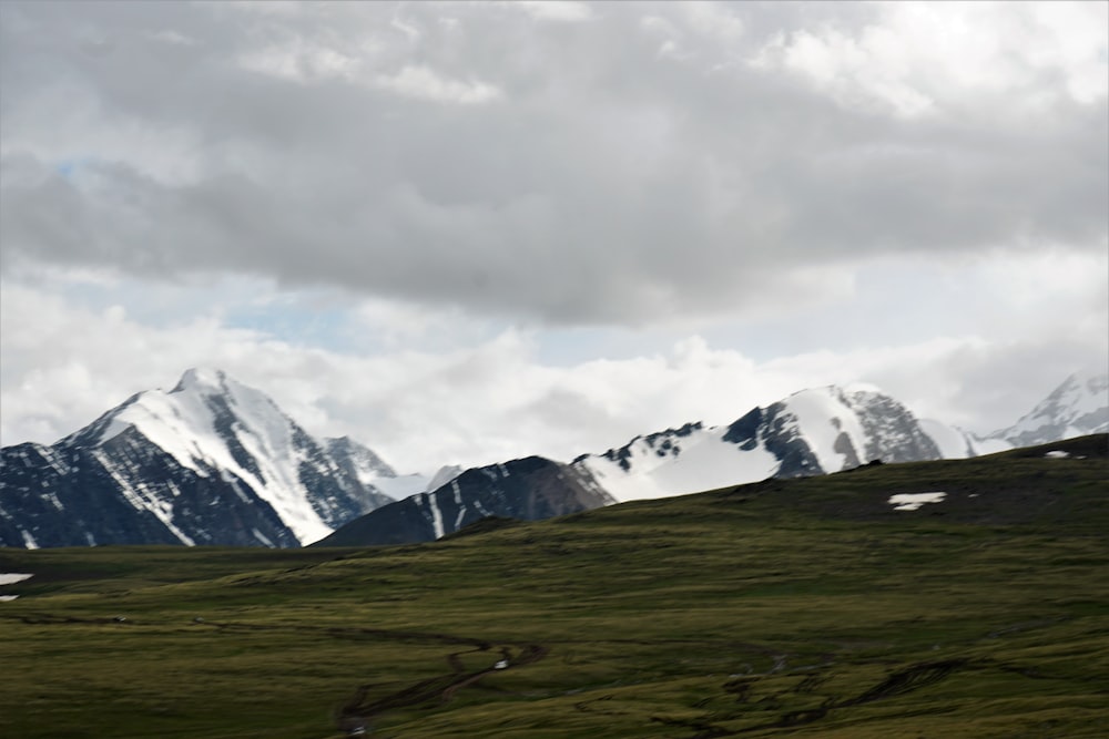 green grass field near snow covered mountain under white cloudy sky during daytime