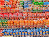 A bright, organized store shelf filled with staple household products like rice, sugar, and instant noodles.