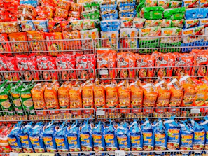 A bright, organized store shelf filled with staple household products like rice, sugar, and instant noodles.