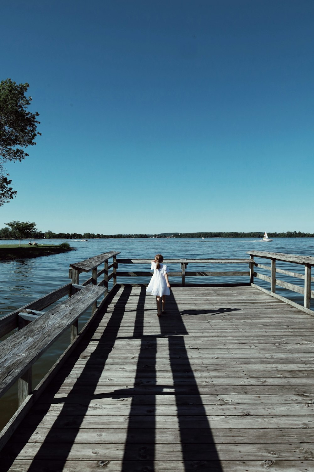 昼間、木製の桟橋に立つ白いドレスを着た女性