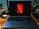 A laptop on a wooden desk with the Netflix logo prominently displayed on its screen. The area is well-organized, featuring a desk lamp, a container holding a variety of pens and pencils, and several cords. The setting suggests a workspace that combines functionality with entertainment.