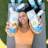 A person is holding two cans of 'Positive Beverage' labeled with flavors 'Mandarin Orange' and 'Crisp Cucumber.' The individual is lying on a yoga mat outdoors, wearing an orange sports top. Other cans are scattered in the background on the grass.