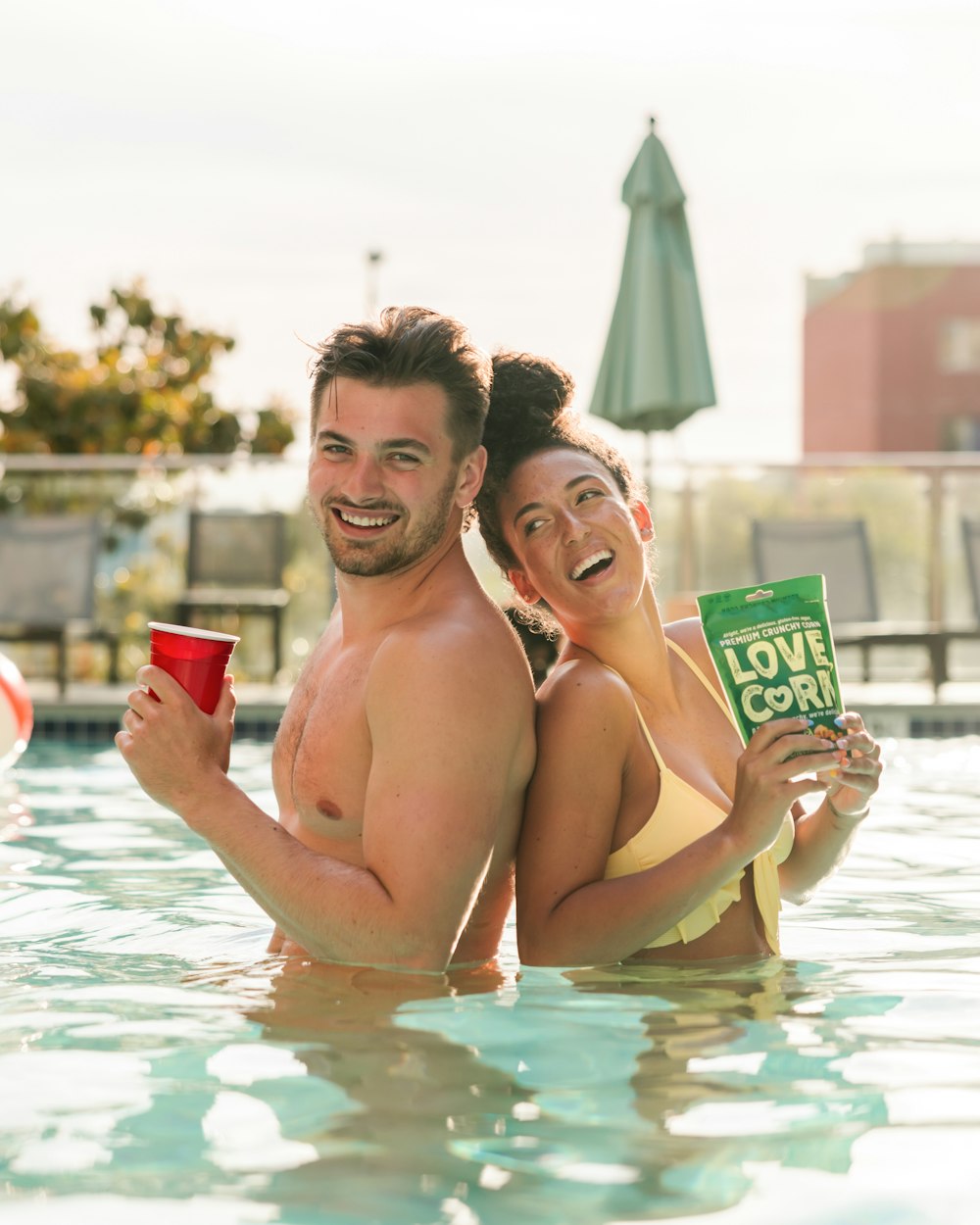 topless man and woman in swimming pool holding green cup during daytime