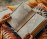 person reading book on brown and beige textile