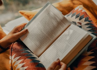 person reading book on brown and beige textile