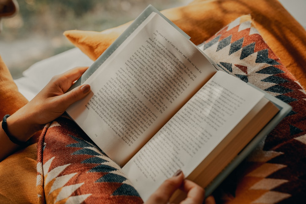 person reading book on brown and beige textile