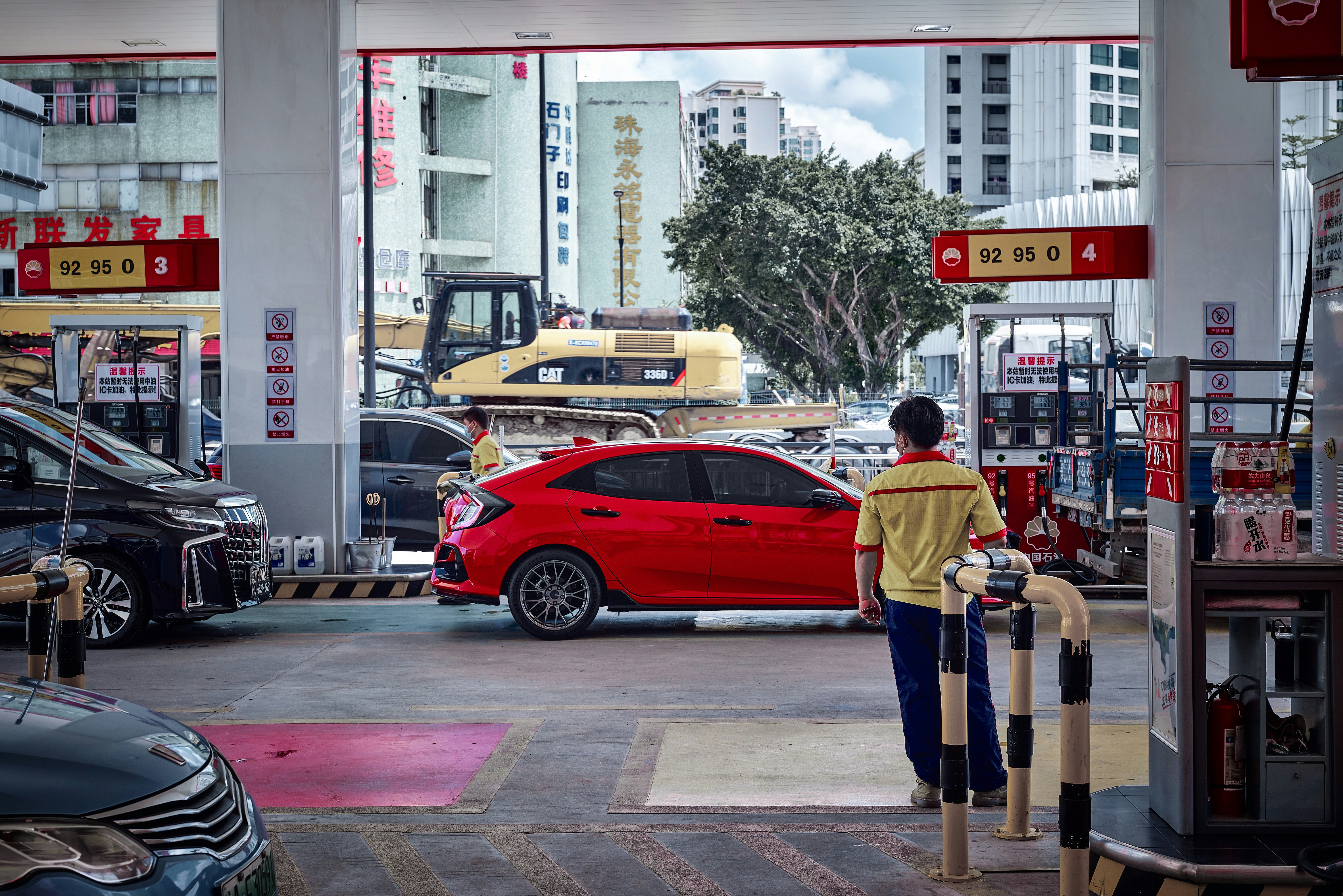 Pria berjaket kuning berdiri di dekat mobil merah di siang hari