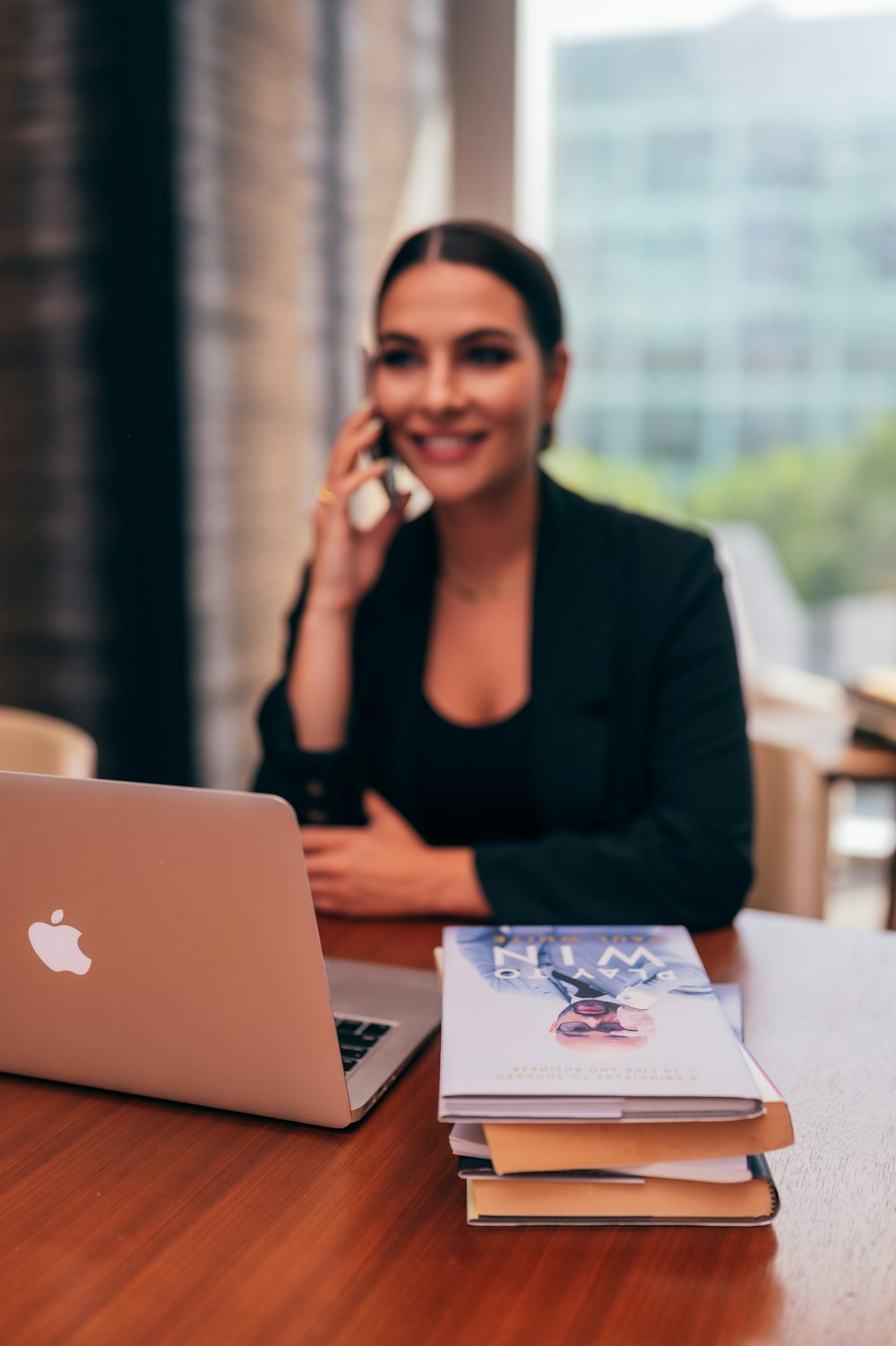 mulher no blazer preto sentado ao lado da mesa com macbook