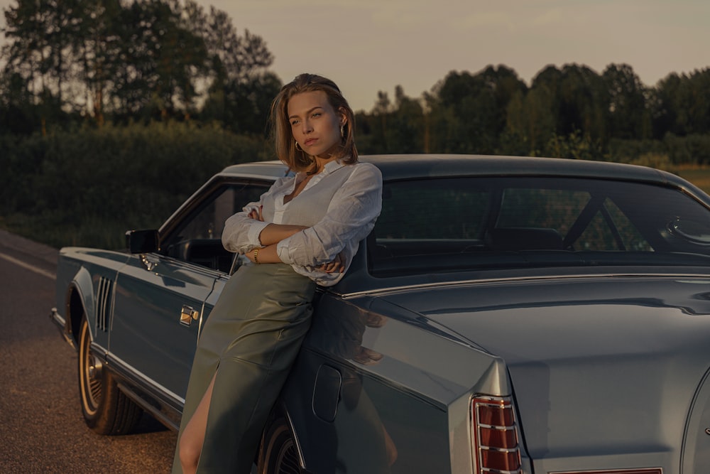 Femme en blazer gris et pantalon assis sur une voiture noire