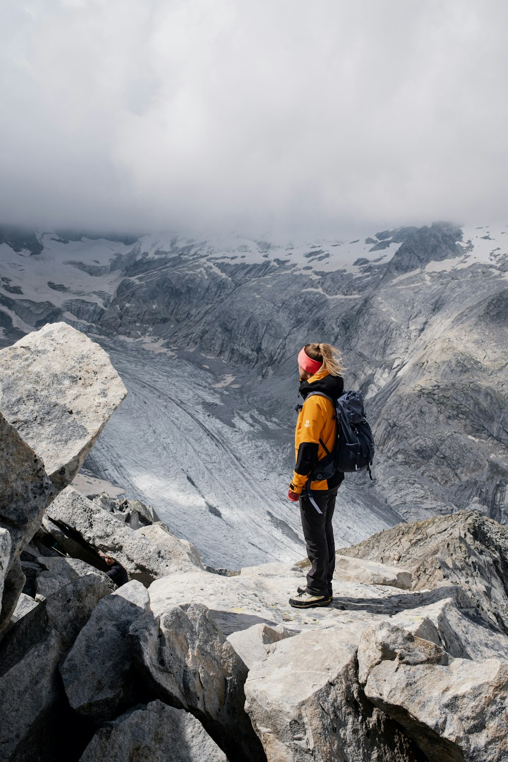 homme en veste orange debout sur la montagne rocheuse pendant la journée