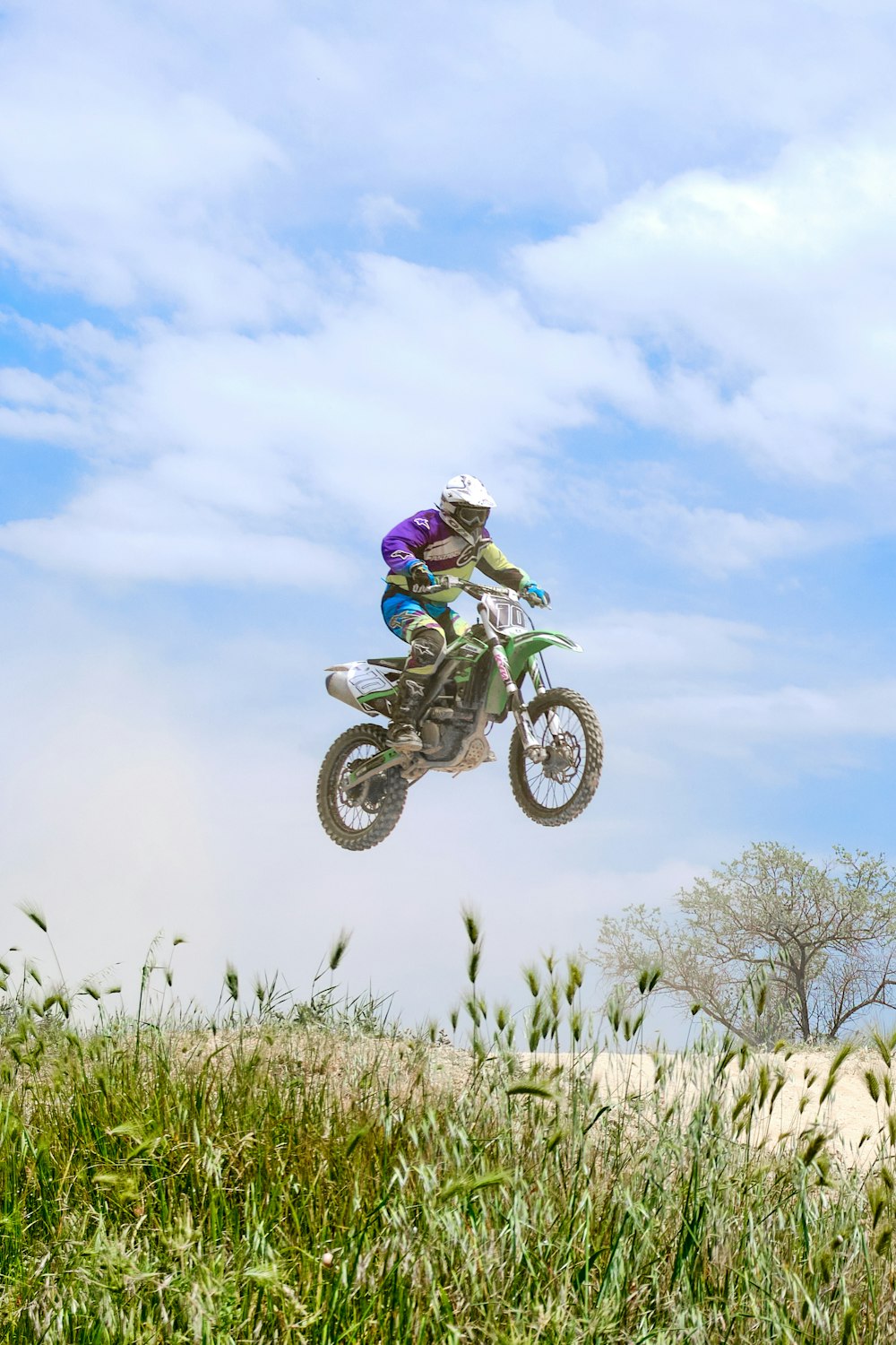 man riding motocross dirt bike on green grass field under white clouds and blue sky during