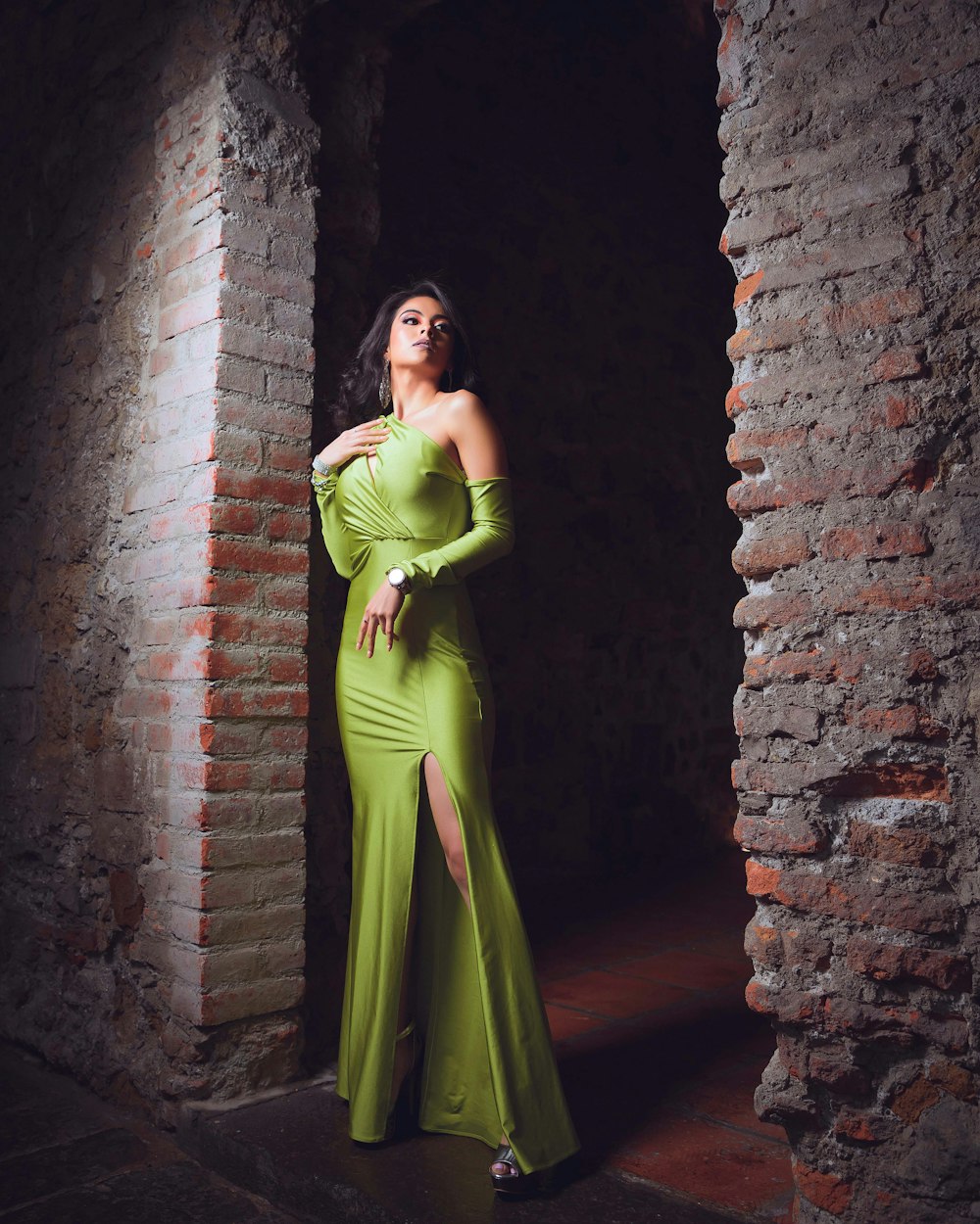 woman in green sleeveless dress leaning on brown brick wall