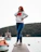 Photo of a confident woman standing on a dock with cargo ships in the background.