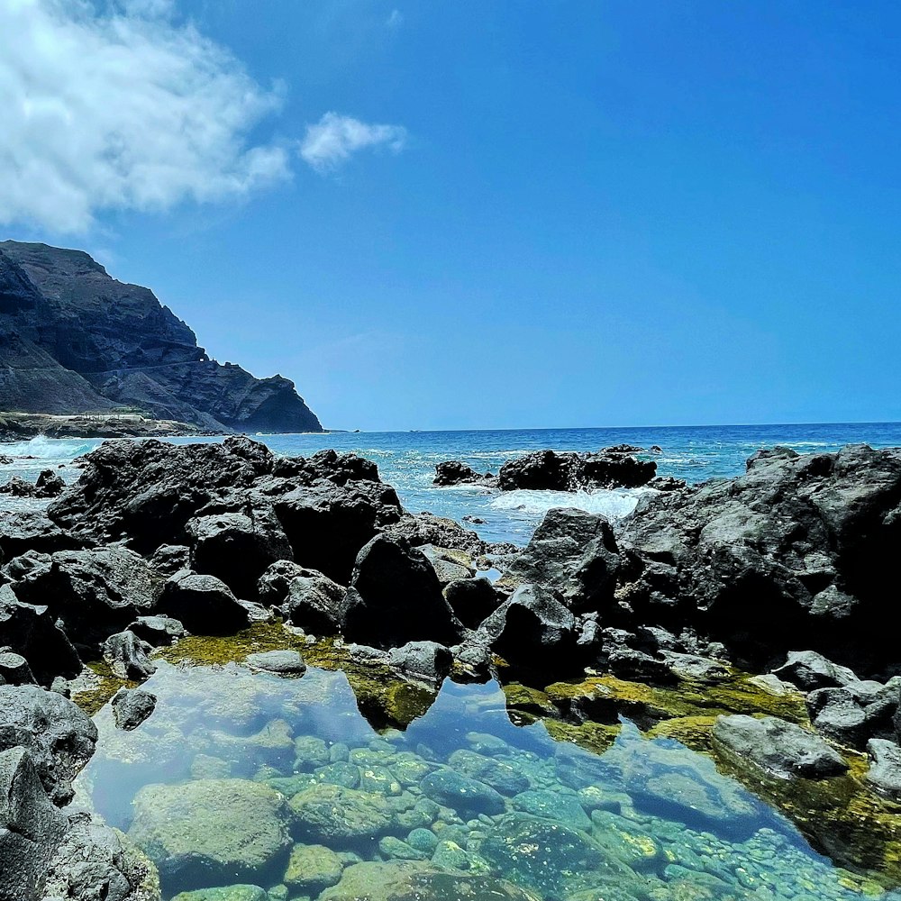 rocky shore with rocky mountain in distance under blue sky with white clouds during daytime