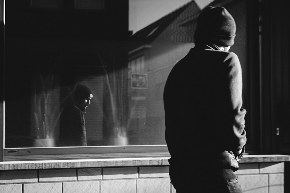 man in black hoodie standing in front of glass window