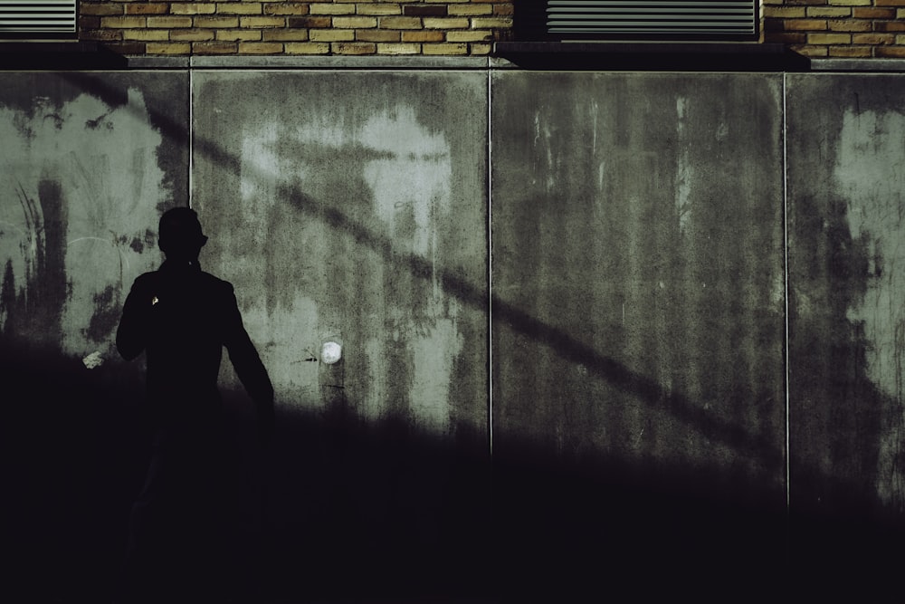 silhouette of man standing beside brick wall