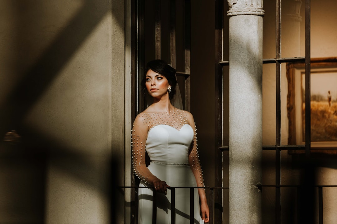 woman in white tube dress wearing black hat standing beside white wall