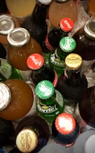 A collection of various bottled beverages placed on ice, featuring brands like Coca-Cola, Sprite, and Stewart’s. The bottles display vibrant caps with brand logos.