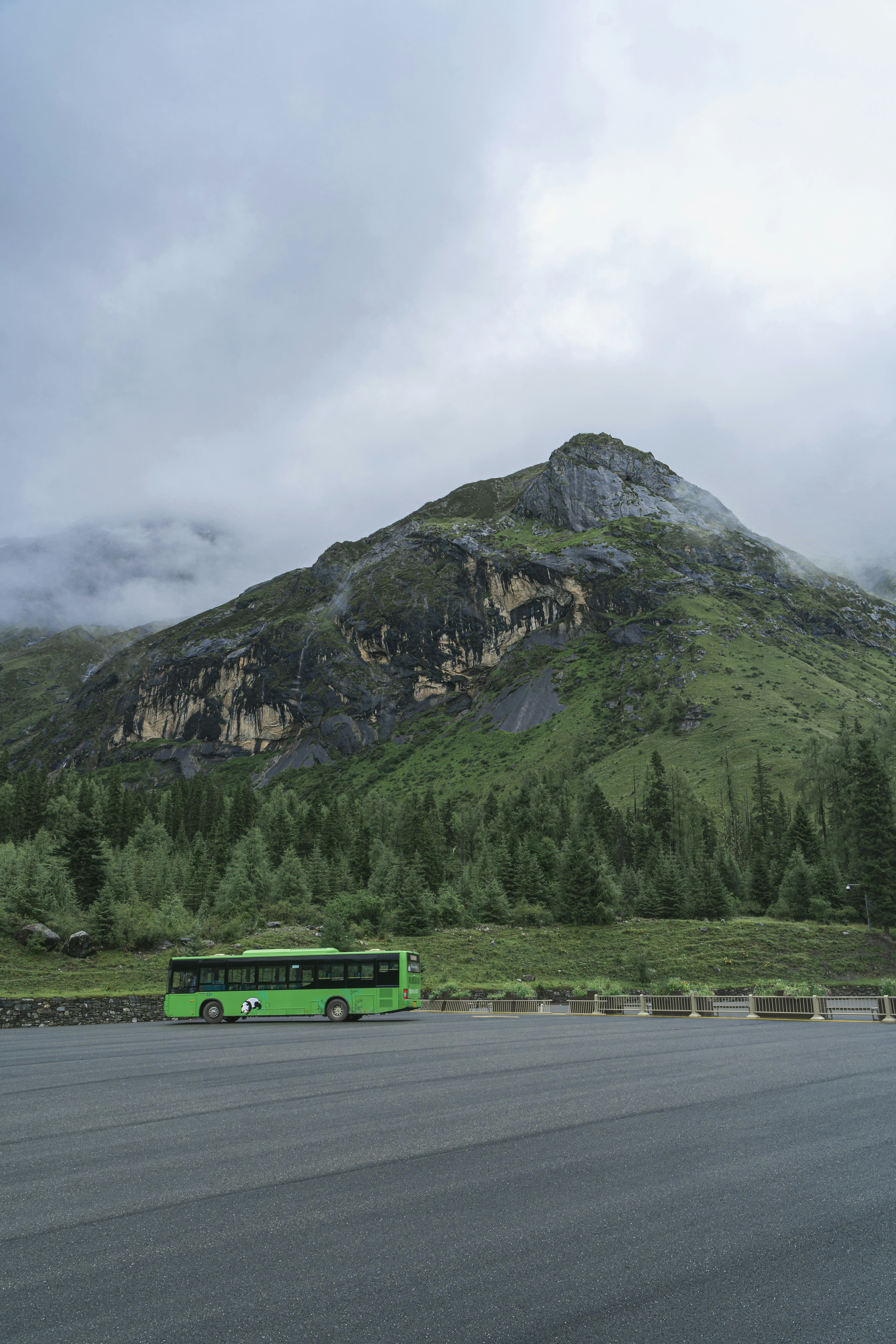 Green tour bus parked on asphalt before mountain slopes.