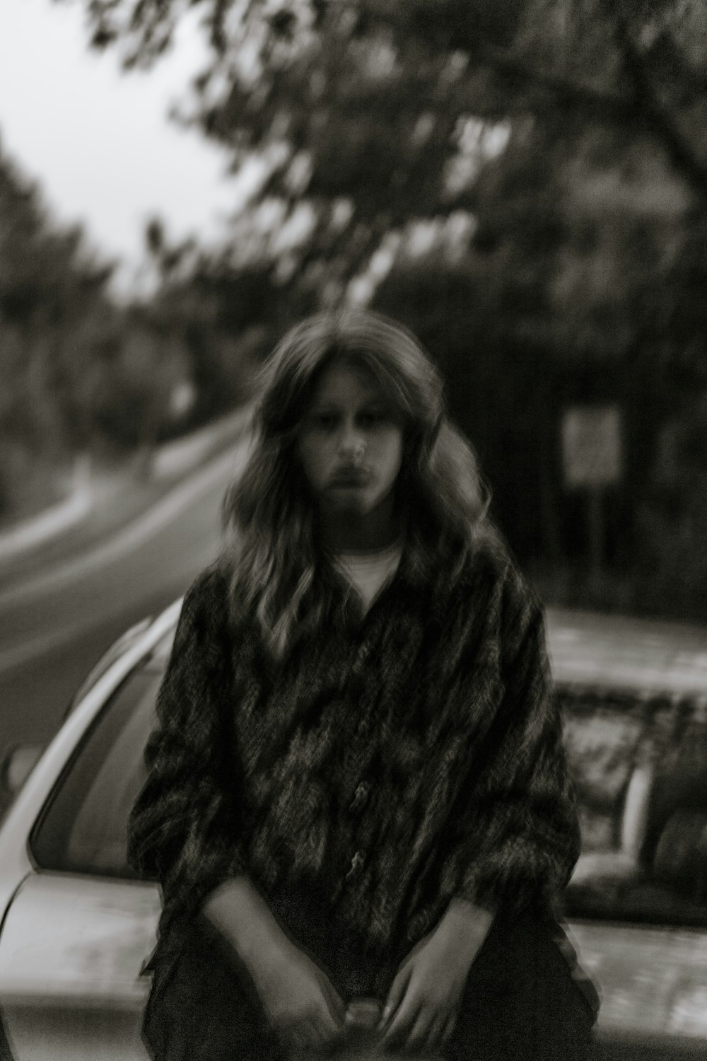 grayscale photo of woman in black and white fur coat standing on road