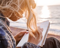 woman in blue and white floral shirt holding book near body of water during daytime