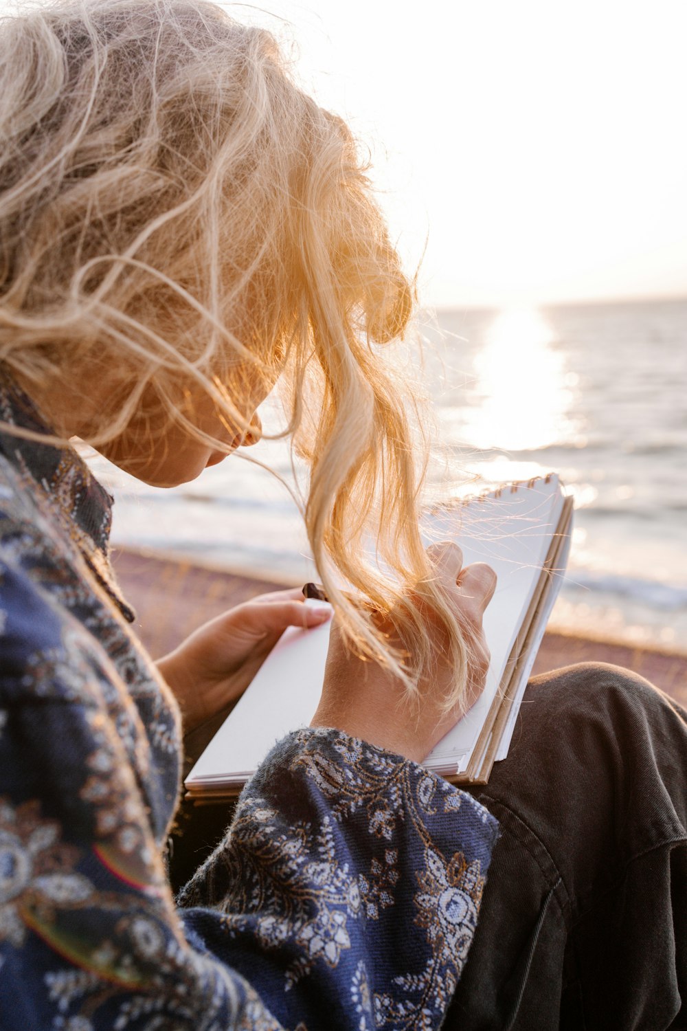 woman in blue and white floral shirt holding book near body of water during daytime