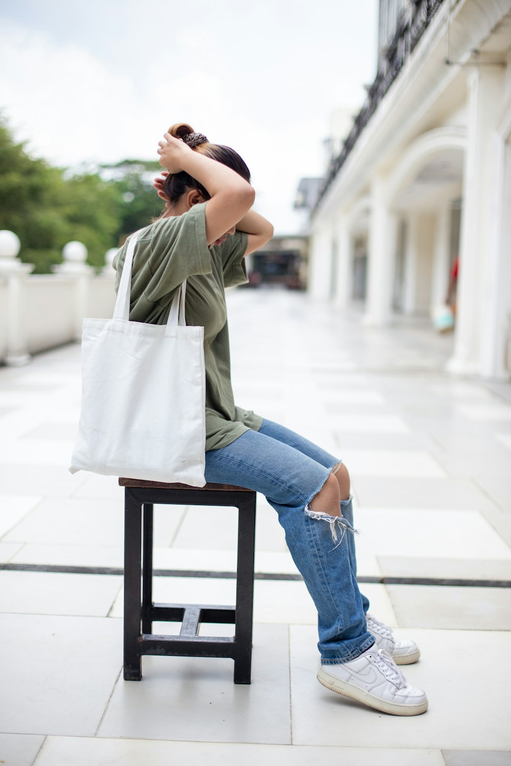 Mujer con chaqueta gris y jeans de mezclilla azul sentada en una silla de madera marrón