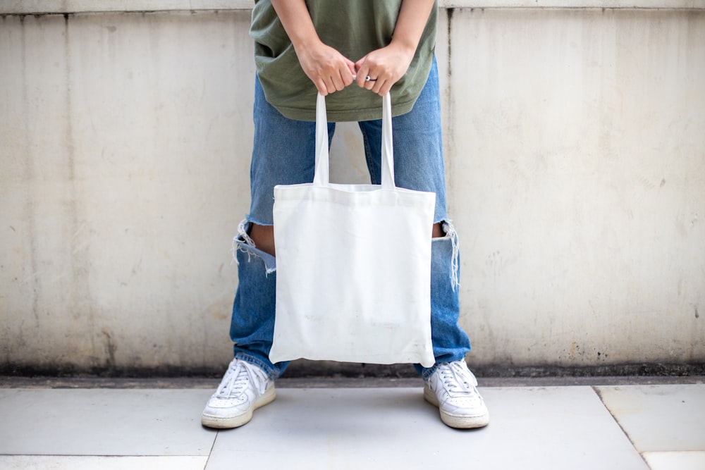 Persona en jeans de mezclilla azul sosteniendo una bolsa de mano blanca