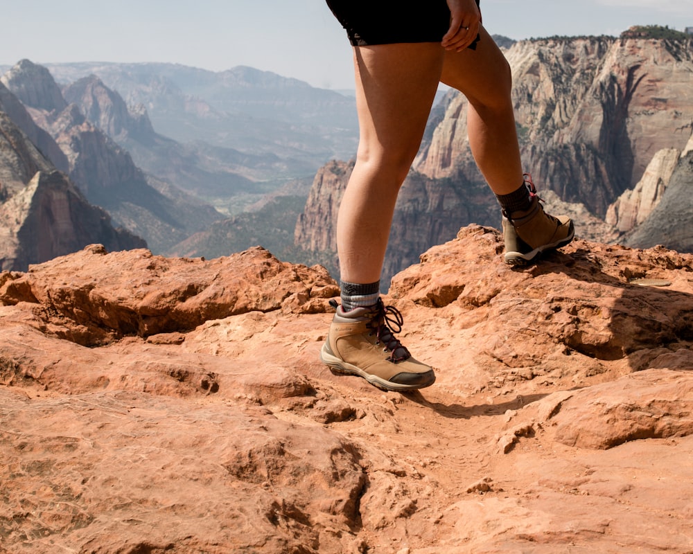 person in black shorts and gray and white sneakers standing on brown rock formation during daytime