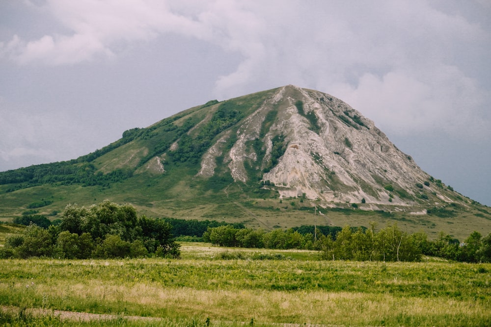 green grass field near mountain under white clouds during daytime