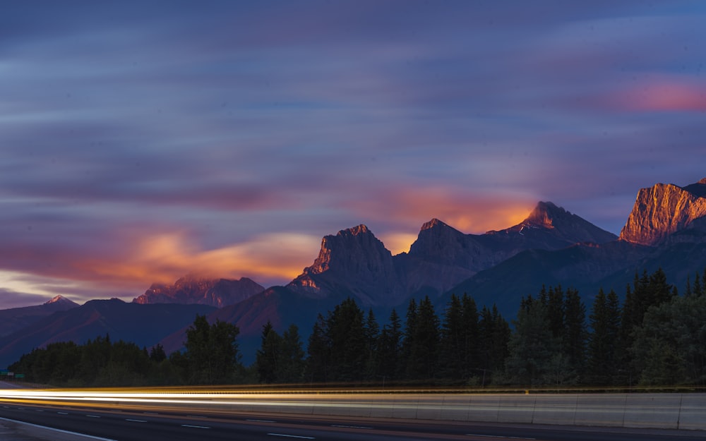 gray asphalt road near green trees and mountains during daytime