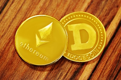 Two shiny cryptocurrency coins, one labeled Ethereum with its logo and the other labeled Dogecoin with its 'D' logo. They rest on a wooden surface.