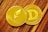 Two shiny cryptocurrency coins, one labeled Ethereum with its logo and the other labeled Dogecoin with its 'D' logo. They rest on a wooden surface.