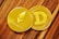 Two shiny cryptocurrency coins, one labeled Ethereum with its logo and the other labeled Dogecoin with its 'D' logo. They rest on a wooden surface.
