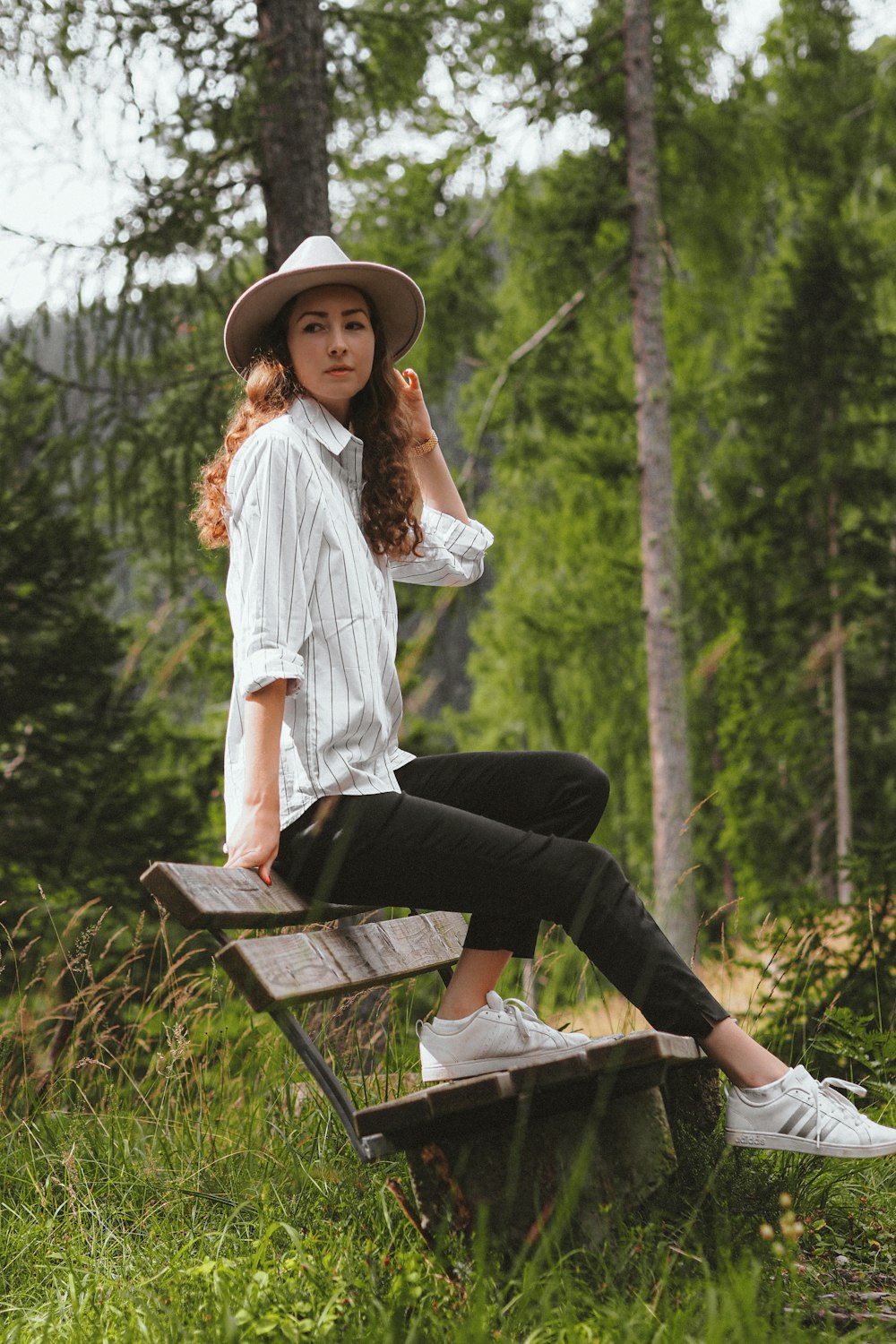 woman in white dress shirt and black pants sitting on brown wooden bench