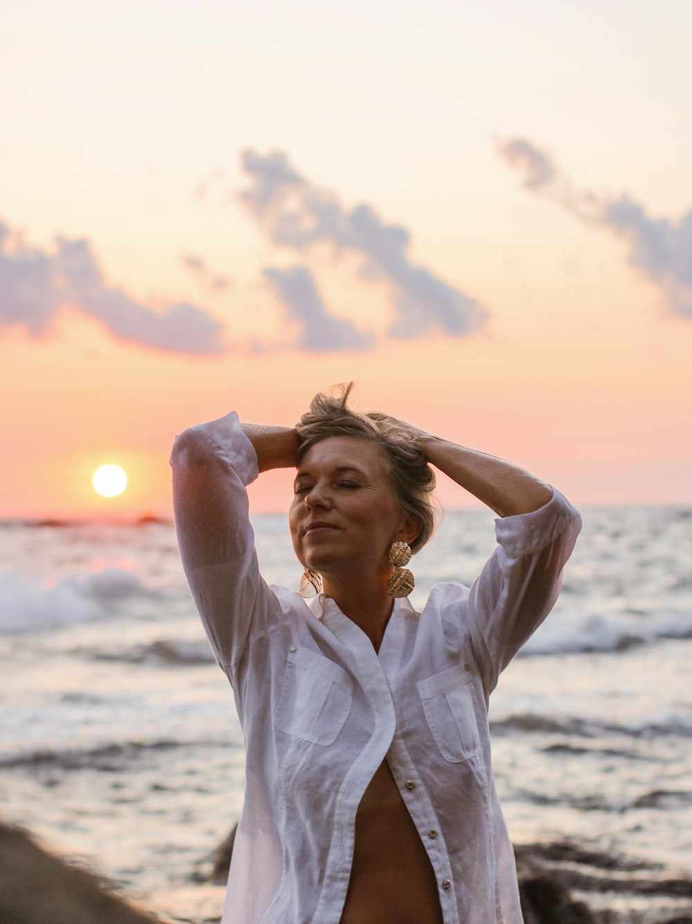 woman in white button up shirt standing on beach during sunset