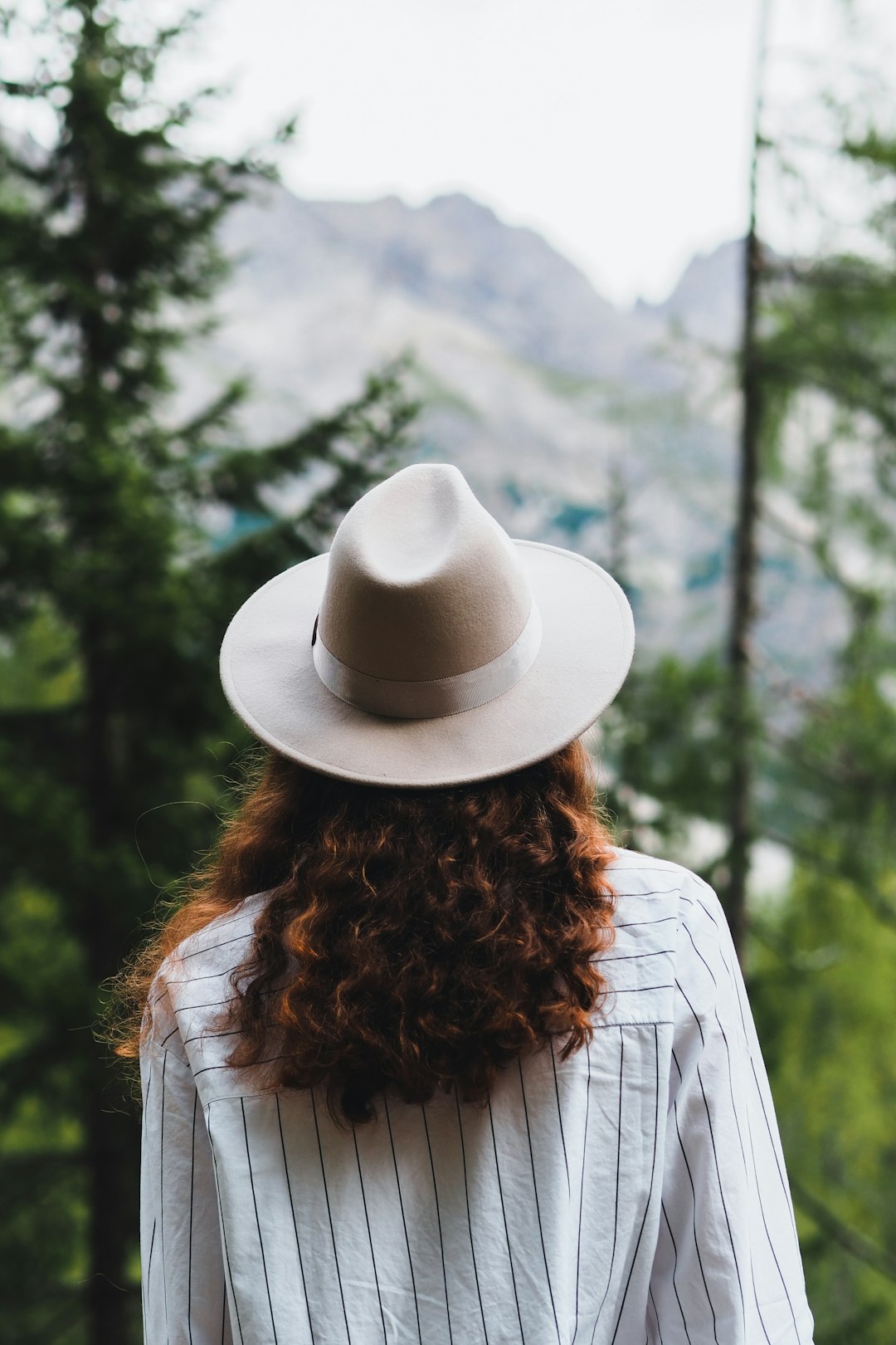 woman in white cowboy hat standing near green trees during daytime