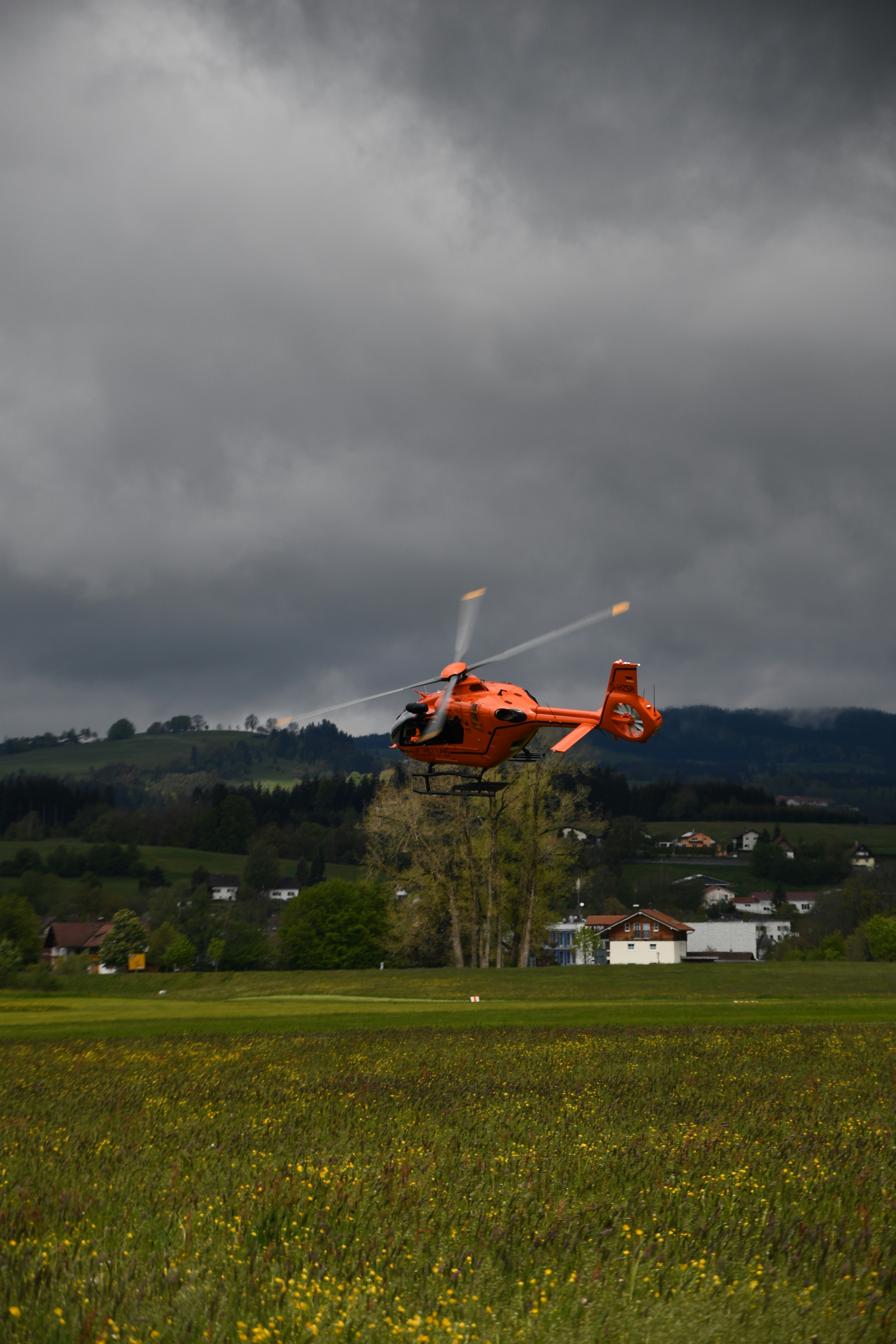red and white helicopter flying over green grass field during daytime