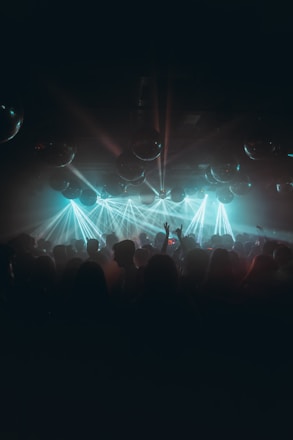 A dimly lit nightclub filled with a crowd of people dancing and enjoying themselves, illuminated by vibrant blue and green laser lights. Reflective disco balls hang from the ceiling, adding to the festive atmosphere.