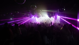 A vibrant nightclub scene with a crowd of people dancing under multicolored laser lights. Numerous disco balls hang from the ceiling, reflecting the illumination, creating a lively and energetic atmosphere.