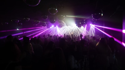 A vibrant nightclub scene with a crowd of people dancing under multicolored laser lights. Numerous disco balls hang from the ceiling, reflecting the illumination, creating a lively and energetic atmosphere.
